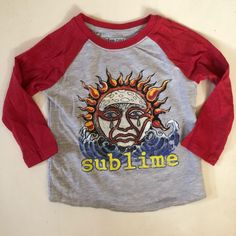 a grey and red shirt with a sun face on the front that says subline