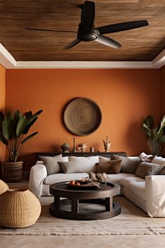 a living room with an orange wall and ceiling fan in the center, white couches on either side