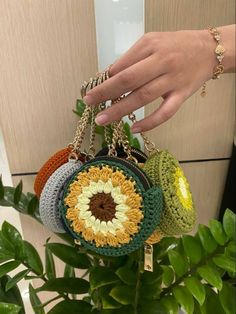 a hand holding a multicolored crocheted purse over a potted plant