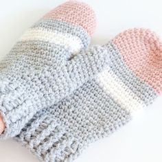 a pair of knitted mittens laying on top of a white table next to a hand