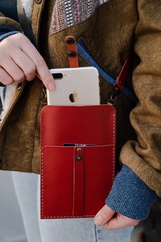 a person holding a cell phone in a red leather case with an attached belt and wrist strap