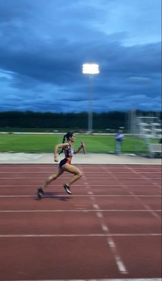 a woman is running on a track at night with the sky in the back ground