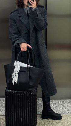 a woman standing in front of an elevator holding a cell phone and carrying a black purse