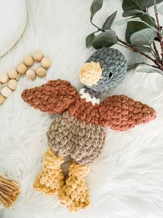 a crocheted stuffed bird sitting on top of a white blanket next to some nuts