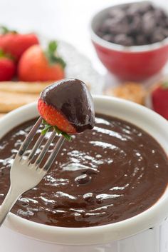 a spoonful of chocolate pudding with a strawberry on top and some strawberries in the background