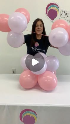 a woman standing behind a table with pink and white balloons in the shape of flowers