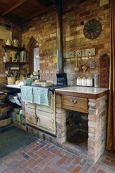 an old fashioned kitchen with brick walls and a wood burning stove in the middle of it