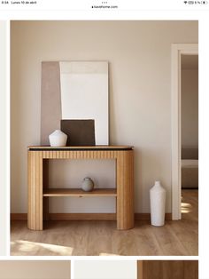 a white vase sitting on top of a wooden table next to a wall mounted painting