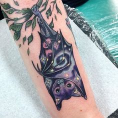 a bat tattoo on the arm with leaves