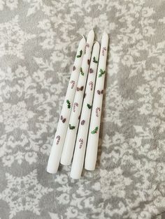 four white candles sitting on top of a bed next to each other with holly designs