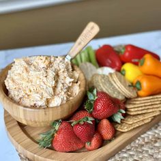 a wooden bowl filled with food next to crackers and strawberries on a plate