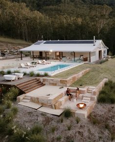 two people are sitting around a fire pit in front of a house with a swimming pool