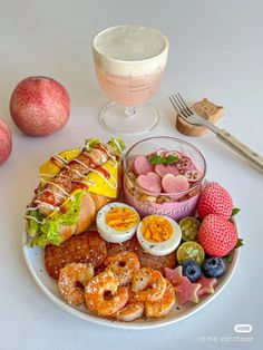 a white plate topped with lots of food next to fruit and a glass of wine