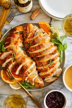 sliced chicken on a plate with oranges, cranberry sauce and wine in the background