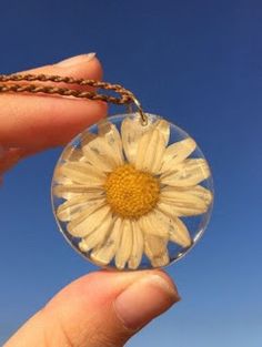 a hand holding a glass ball with a yellow flower inside it and a chain attached to it