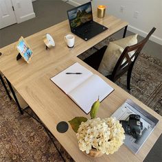 a laptop computer sitting on top of a wooden desk next to a vase with flowers