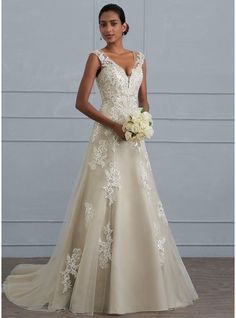 a woman in a wedding dress standing next to a white wall and holding a bouquet