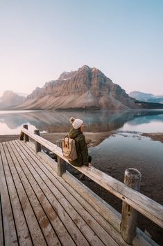 a person sitting on a bench looking out at the water and mountains in the distance