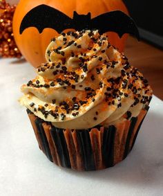 a cupcake with sprinkles and a bat on top sits next to a pumpkin