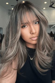 This hairstyle showcases a layered cut with voluminous, tousled waves, emanating a relaxed yet stylish aura. The ash blonde base is skillfully accented with subtle, sun-kissed highlights, adding depth and dimension to the overall look. The face-framing highlights, especially around the bangs, draw attention to the eyes and soften the - Click to see more of Upgrade Your Look with 36 Stunning Hair Highlight Picks and follow us for more hairstyle ideas. // Photo Credit: Instagram @hairbyjess_1 Hair Color With Bangs Highlights, Ash Blonde Balayage With Bangs, Ash Blonde Highlights Dark Hair, Blonde And Ash Highlights, Brunette Hair Ash Highlights, Ashy Grey Highlights, Blonde With Grey Highlights, Blended Gray Hair With Highlights, Bangs With Blonde Highlights