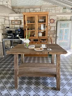 a wooden table sitting inside of a kitchen next to a counter top with plates and cups on it