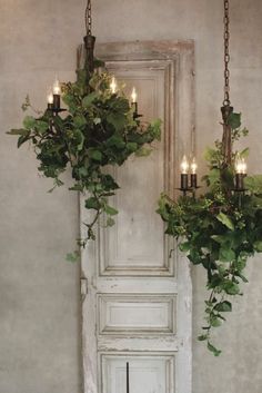 two hanging planters filled with green plants next to a white door that has candles on it