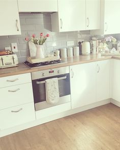 a kitchen with white cabinets and wood flooring is pictured in this image, there are flowers on the stove