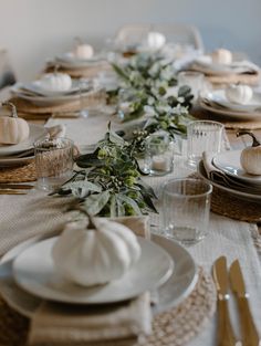 the table is set with white pumpkins and greenery