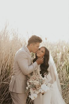 a newly married couple kissing in front of tall grass and flowers on their wedding day