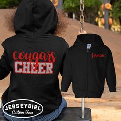 a person sitting on a bench wearing a black jacket with the words cougar's cheer printed on it