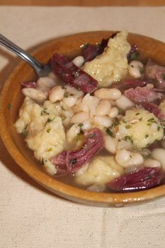 a bowl filled with meat and beans on top of a white table cloth next to a spoon