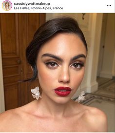 a woman with red lipstick and flower earrings on her head is looking at the camera