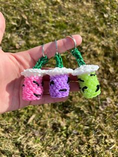 someone is holding three small crocheted key chains in their hand, each with different colored yarns