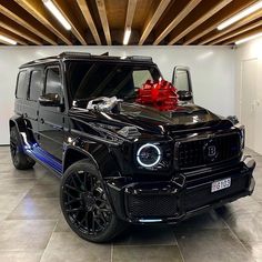 a black mercedes g - class with a red bow on the hood is parked in a garage