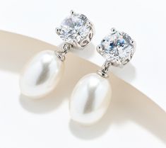 a pair of pearl and diamond earrings on top of a white surface with shadows from the background