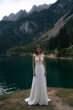 a woman in a wedding dress standing on the edge of a lake