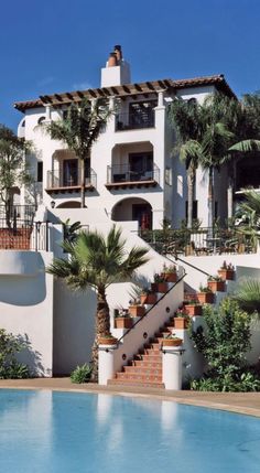 an outdoor swimming pool next to a white building with palm trees on the balconies