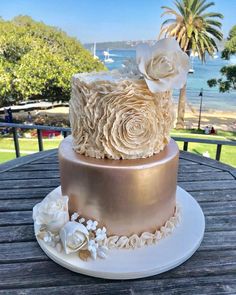 a three tiered cake with white flowers on top sits on a table near the water