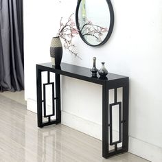 a black console table with two vases and a mirror on the wall behind it