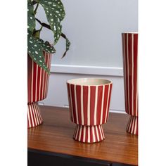 three red and white striped vases sitting on a table next to a potted plant