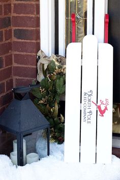 a white sled sitting in front of a door next to a christmas wreath and lantern