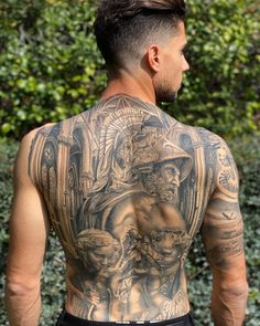 a man with tattoos on his back standing in front of some bushes and trees,