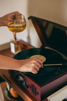 a person holding a record player with a glass in front of it on top of a table