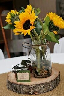 a vase filled with sunflowers sitting on top of a wooden slice at a table