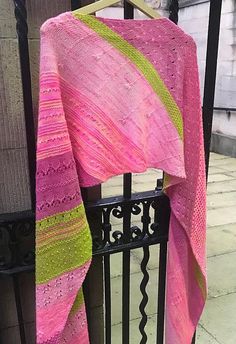 a pink and green shawl is hanging on a fence near a black iron gate