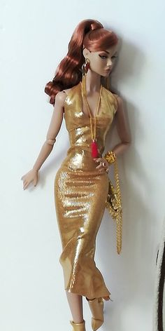 a barbie doll wearing a gold dress and holding a red rose in her hand, leaning against a white wall