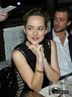 a woman sitting at a table with her hand on her chin, and a man standing next to her