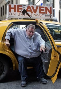 a man sitting in the driver's seat of a yellow car on a city street