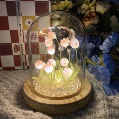 a glass dome with flowers in it on a wooden stand next to a gift box