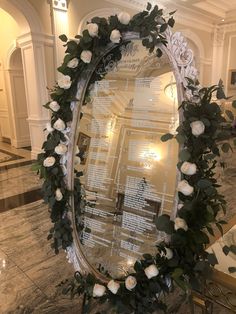 a mirror with flowers and greenery on it in a hotel lobby, surrounded by marble flooring